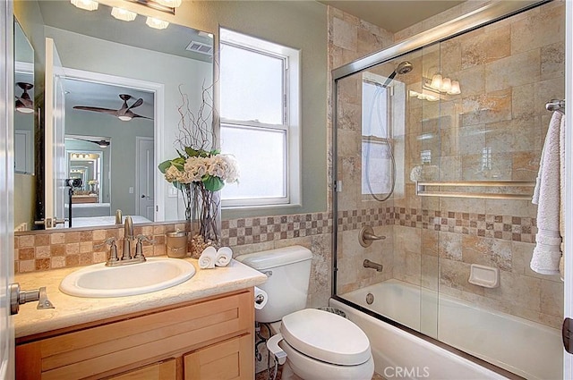 full bathroom with ceiling fan, combined bath / shower with glass door, tile walls, vanity, and toilet