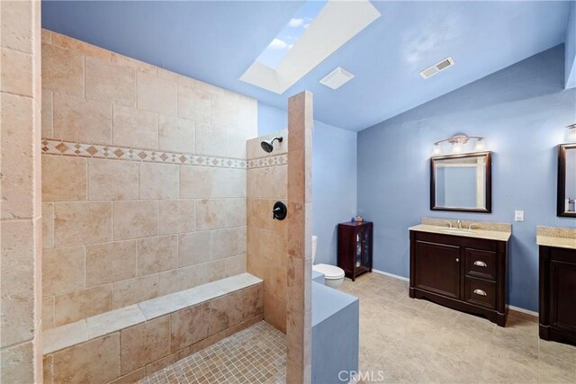 bathroom featuring lofted ceiling with skylight, tiled shower, vanity, and toilet