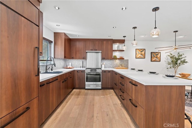 kitchen featuring sink, stainless steel gas stove, light wood-type flooring, paneled refrigerator, and pendant lighting