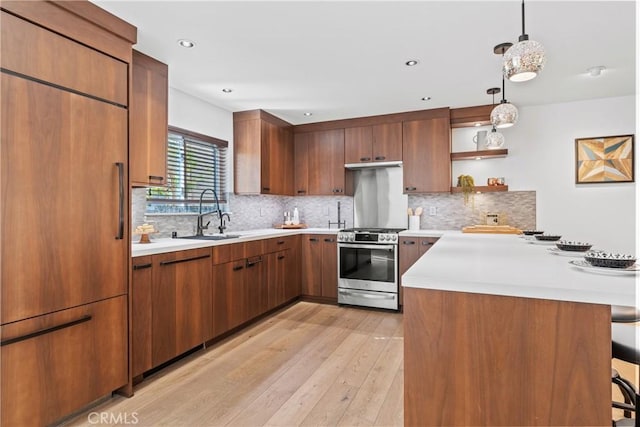 kitchen featuring sink, a breakfast bar area, hanging light fixtures, stainless steel range with gas cooktop, and paneled built in fridge