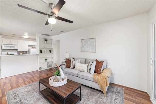 living area with a textured ceiling, dark wood-style flooring, visible vents, and a ceiling fan