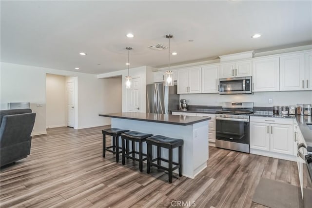 kitchen with a kitchen bar, white cabinetry, hanging light fixtures, appliances with stainless steel finishes, and a kitchen island