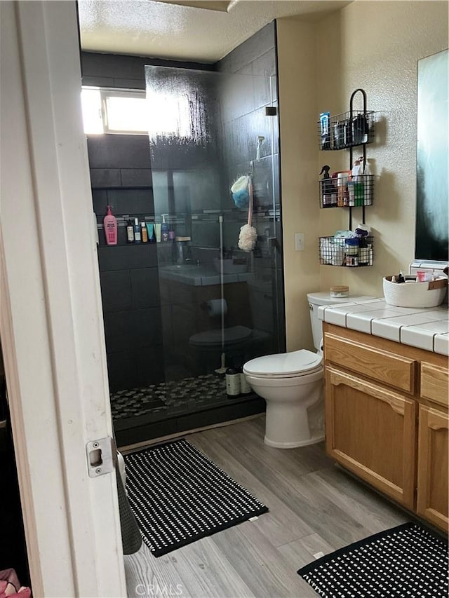 bathroom featuring walk in shower, toilet, wood-type flooring, a textured ceiling, and vanity