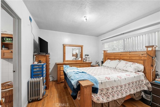 bedroom featuring radiator heating unit, light hardwood / wood-style floors, and a textured ceiling