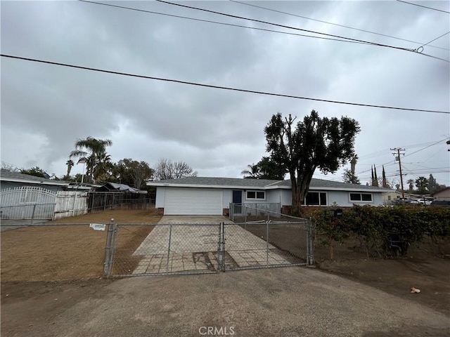 ranch-style home featuring concrete driveway, a fenced front yard, an attached garage, and a gate