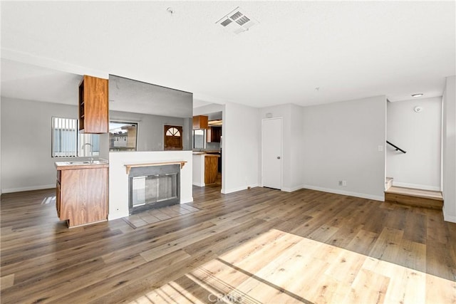 unfurnished living room with visible vents, a sink, baseboards, and wood finished floors