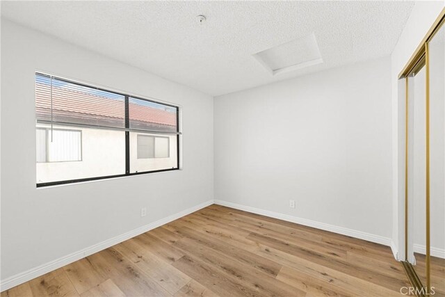 unfurnished room featuring a textured ceiling, light wood-style flooring, attic access, and baseboards