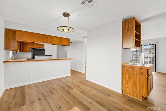 kitchen featuring visible vents, a peninsula, light countertops, pendant lighting, and a sink