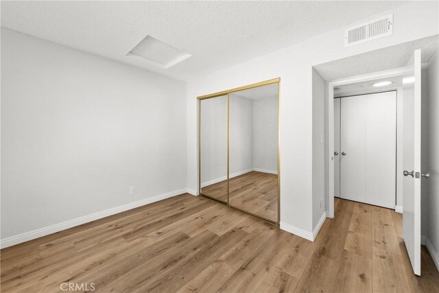 unfurnished bedroom featuring attic access, visible vents, light wood-style flooring, and baseboards