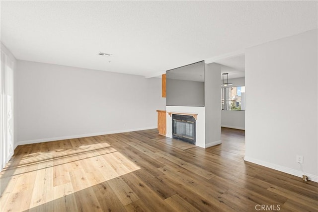 unfurnished living room featuring a glass covered fireplace, wood finished floors, visible vents, and baseboards