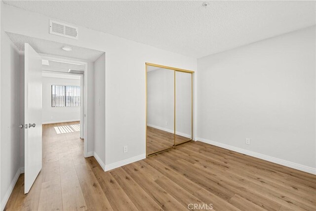 unfurnished bedroom with a closet, visible vents, light wood-style flooring, a textured ceiling, and baseboards