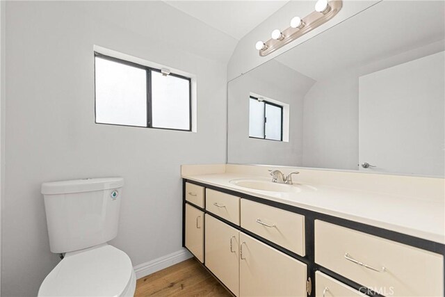 half bath featuring toilet, wood finished floors, vanity, baseboards, and vaulted ceiling