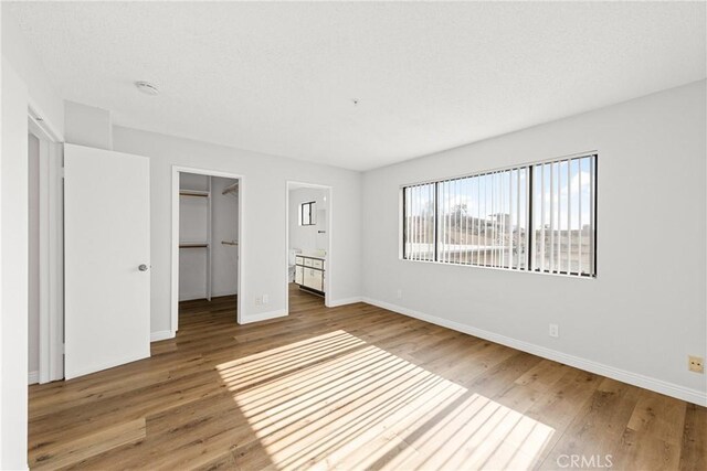 unfurnished bedroom featuring a closet, a spacious closet, baseboards, and wood finished floors