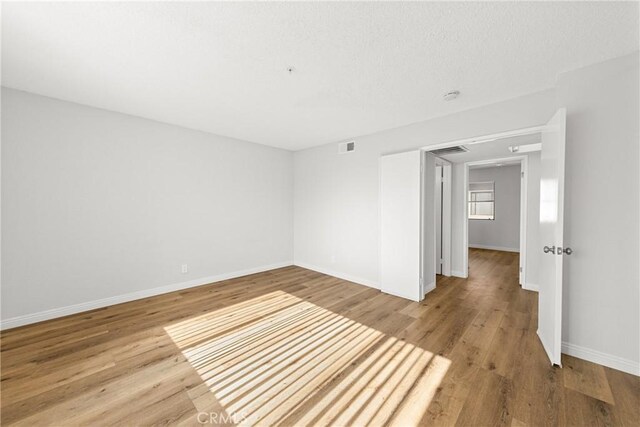 spare room with wood finished floors, visible vents, and baseboards