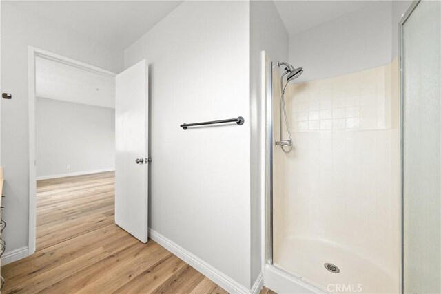 bathroom featuring wood finished floors, a shower stall, and baseboards