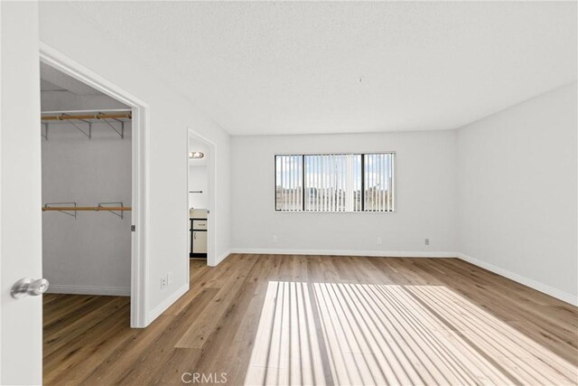 unfurnished bedroom featuring a closet, baseboards, a spacious closet, and light wood finished floors