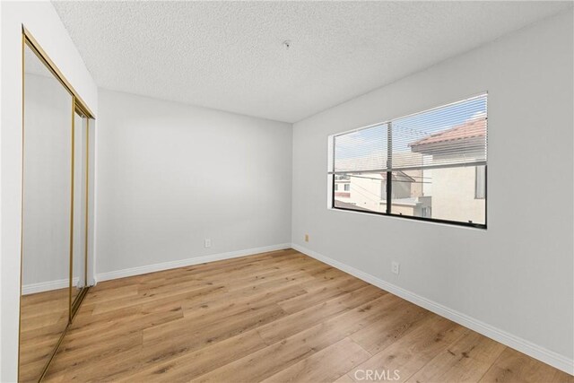 unfurnished bedroom featuring a closet, a textured ceiling, baseboards, and wood finished floors