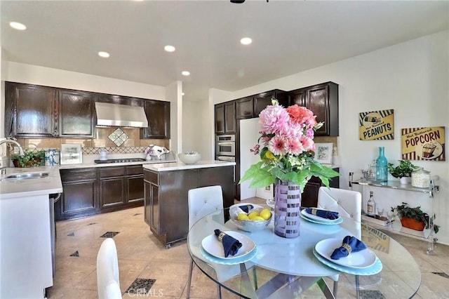 kitchen with appliances with stainless steel finishes, tasteful backsplash, sink, a center island, and wall chimney range hood