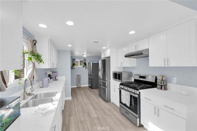 kitchen with sink, light hardwood / wood-style flooring, stainless steel appliances, light stone countertops, and white cabinets