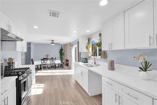 kitchen with sink, stainless steel gas stove, ceiling fan, light stone countertops, and white cabinets