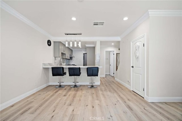 kitchen featuring gray cabinetry, a kitchen breakfast bar, tasteful backsplash, ornamental molding, and kitchen peninsula