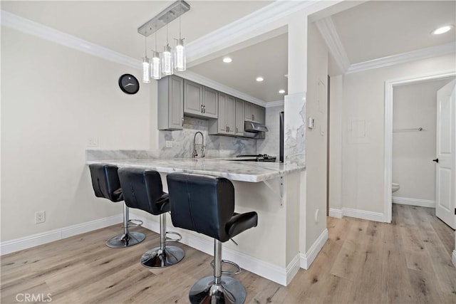 kitchen with a kitchen bar, ornamental molding, gray cabinets, kitchen peninsula, and decorative backsplash