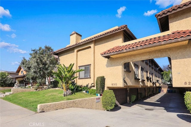 view of property exterior with a garage, driveway, a yard, stucco siding, and a chimney