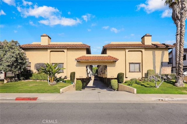 mediterranean / spanish home with a chimney, a front lawn, concrete driveway, and stucco siding