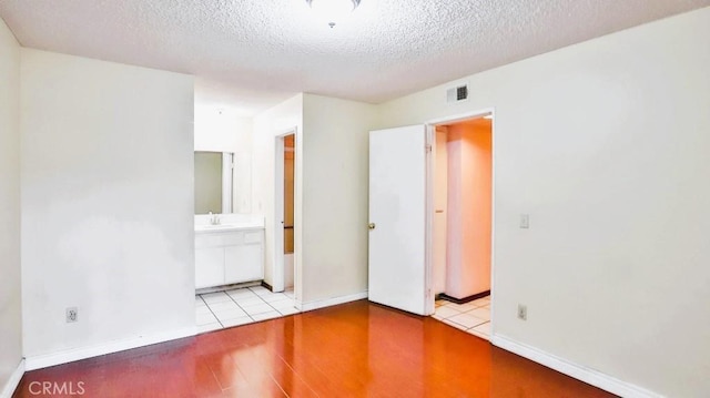 unfurnished bedroom featuring ensuite bath, sink, a textured ceiling, and light hardwood / wood-style floors