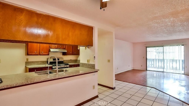 kitchen featuring sink, light tile patterned floors, gas stove, light stone countertops, and a textured ceiling