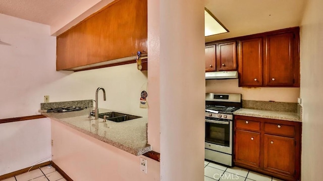 kitchen with sink, light tile patterned floors, light stone counters, gas stove, and kitchen peninsula