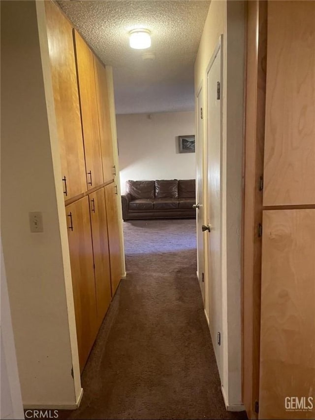 hallway featuring dark carpet and a textured ceiling