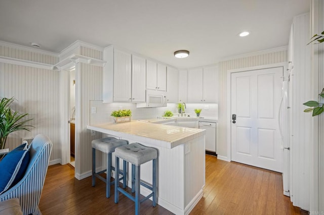 kitchen featuring wood-type flooring, a peninsula, white cabinetry, and white appliances