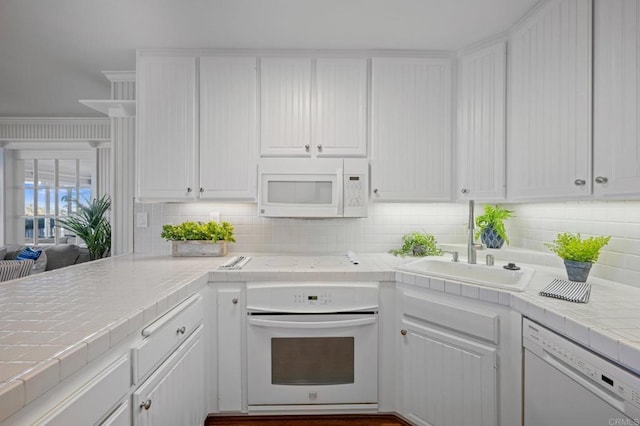 kitchen featuring white cabinets, a sink, tasteful backsplash, white appliances, and tile counters