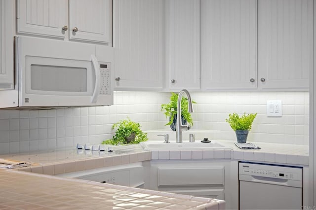 kitchen featuring white cabinets, tile countertops, a sink, white appliances, and decorative backsplash