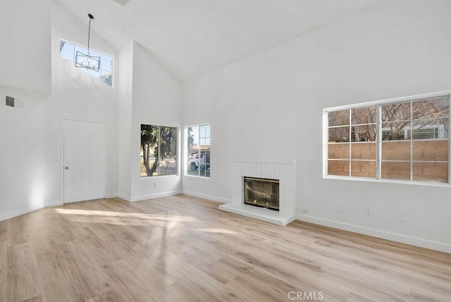 unfurnished living room featuring high vaulted ceiling, light wood-type flooring, a notable chandelier, and a fireplace