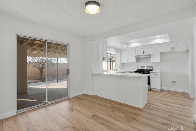 kitchen with stainless steel gas stove, light hardwood / wood-style flooring, kitchen peninsula, and white cabinets