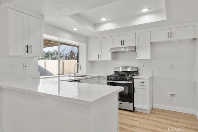 kitchen featuring kitchen peninsula, sink, white cabinets, a tray ceiling, and stainless steel gas range