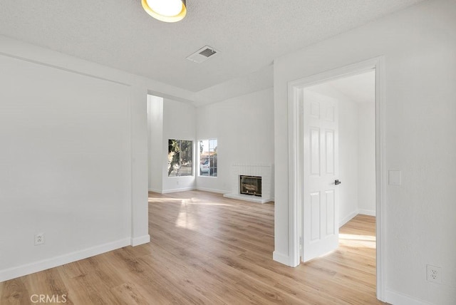 unfurnished living room with light hardwood / wood-style flooring, a fireplace, and a textured ceiling