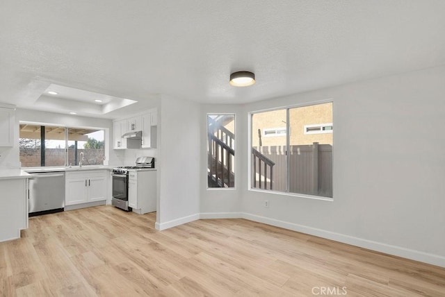 kitchen featuring sink, stainless steel appliances, white cabinets, a raised ceiling, and light wood-type flooring