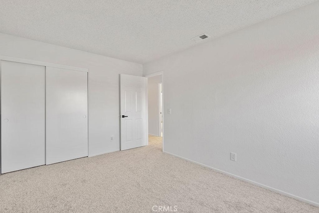 unfurnished bedroom with light colored carpet, a closet, and a textured ceiling