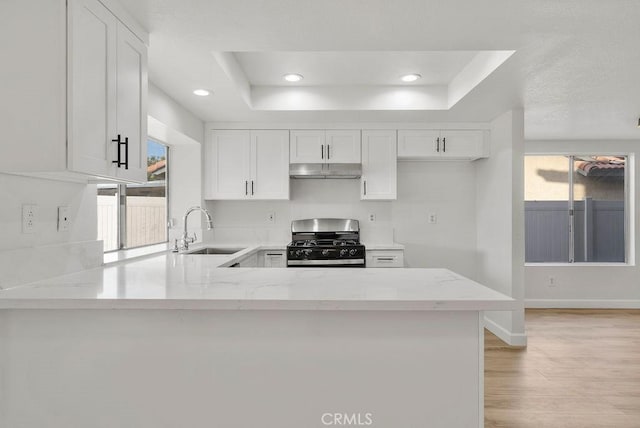 kitchen with sink, stainless steel range with gas stovetop, light stone counters, white cabinets, and kitchen peninsula