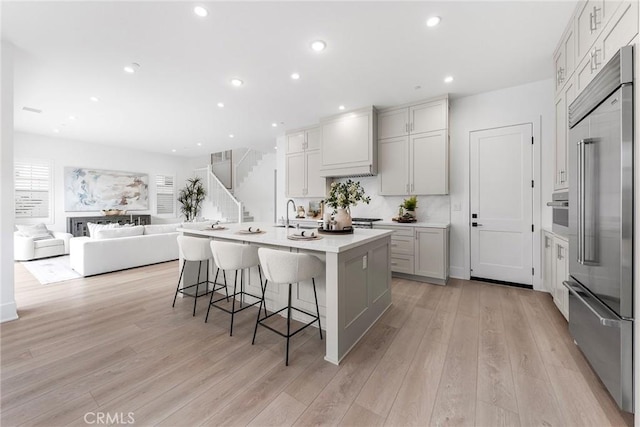 kitchen featuring stainless steel built in refrigerator, a breakfast bar area, a center island with sink, and light wood-type flooring