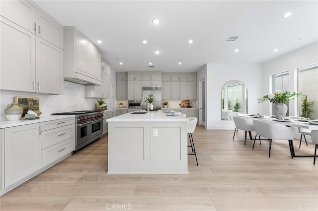 kitchen featuring a kitchen bar, sink, light hardwood / wood-style flooring, high quality appliances, and a kitchen island with sink