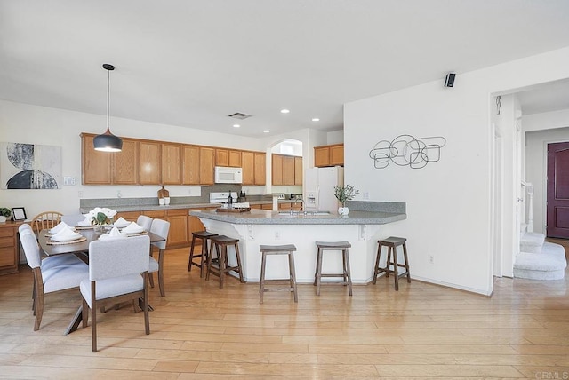 kitchen with a breakfast bar, hanging light fixtures, kitchen peninsula, white appliances, and light hardwood / wood-style floors