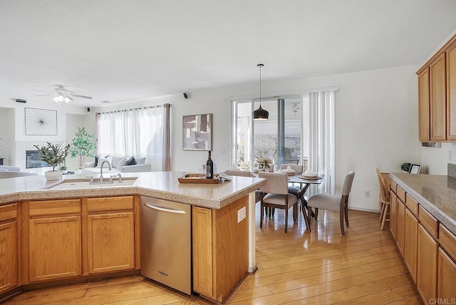 kitchen featuring sink, decorative light fixtures, light hardwood / wood-style flooring, ceiling fan, and a tiled fireplace