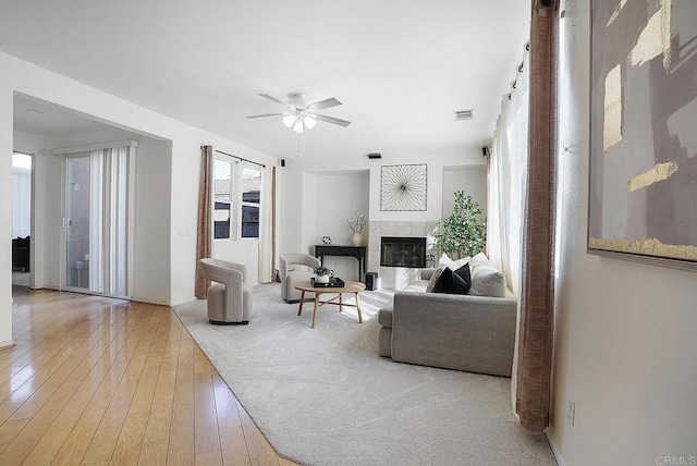 living room featuring ceiling fan, plenty of natural light, a fireplace, and light hardwood / wood-style floors