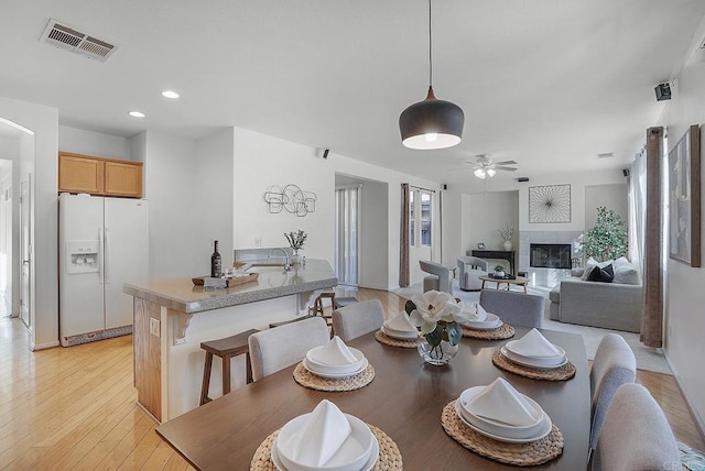 dining room featuring ceiling fan, a tiled fireplace, and light hardwood / wood-style flooring