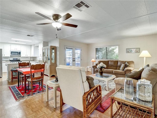 living area featuring a ceiling fan, french doors, visible vents, and a textured ceiling