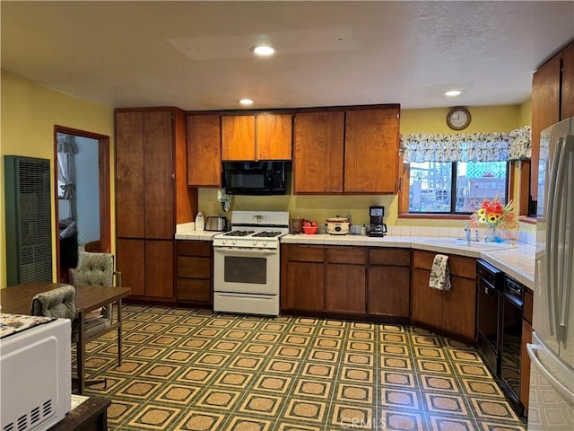 kitchen with brown cabinets, freestanding refrigerator, gas range gas stove, black microwave, and a sink